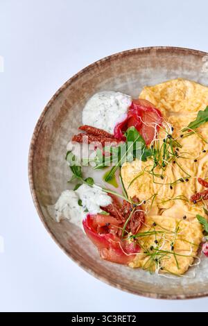 Delizioso piatto gourmet con soffici uova strapazzate abbinate a salmone affumicato, verdure fresche, salsa cremosa e pomodori secchi, perfetto per un He Foto Stock