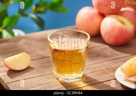 Sidro di mele frizzante in un bicchiere con mele fresche su un tavolo di legno, bicchiere di succo di mela su un tavolo di legno in giardino, vista ravvicinata Foto Stock
