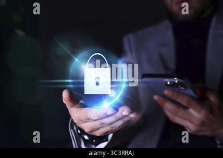 Immagine di una persona irriconoscibile che guarda il proprio telefono cellulare con un'icona con un lucchetto in mano. Concetto di sicurezza informatica online Foto Stock