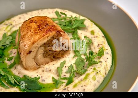 Involtino di pollo realizzato con gusto su un letto cremoso di purè di patate con contorno di rucola fresca che mostra arte culinaria e presentazione saporita Foto Stock