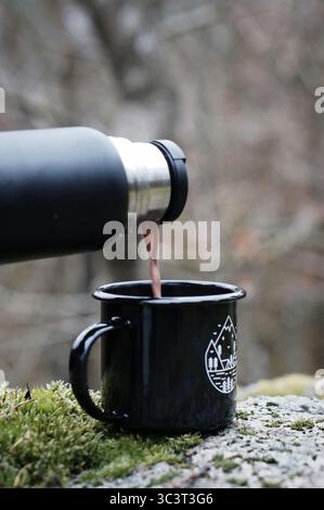 la bevanda calda viene versata da un thermos in una tazza all'aperto nella foresta Foto Stock