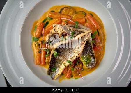 Un delizioso piatto con pesce appena cucinato, carote vivaci e una salsa cremosa, sapientemente organizzata per una squisita esperienza culinaria. Foto Stock