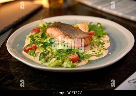 Filetto di salmone deliziosamente grigliato servito su un letto di verdure fresche con salsa cremosa e pomodori ciliegini per un'esperienza culinaria saporita Foto Stock
