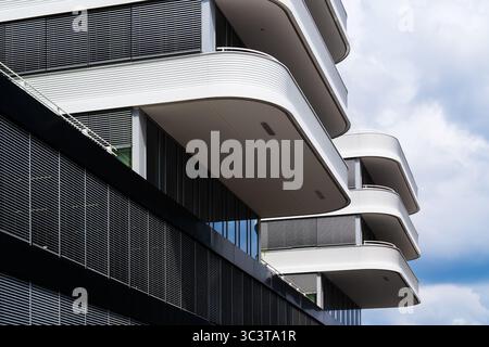 Facciata residenziale contemporanea con balconi bianchi curvi e tonalità ritmiche del sole Foto Stock