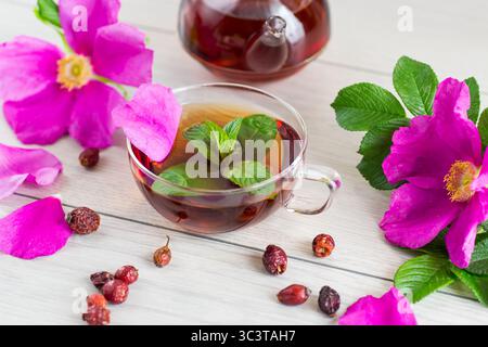 Tè alla menta e rosehip curativo in tazza e teiera dall'alto su un tavolo di legno chiaro. Foto Stock