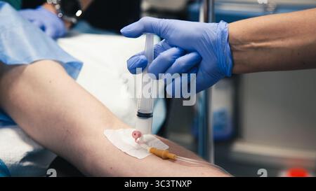 L'operatore sanitario con guanti blu sta prelevando sangue dal braccio di un paziente con una siringa, evidenziando la professionalità e l'atmosfera clinica del farmaco Foto Stock