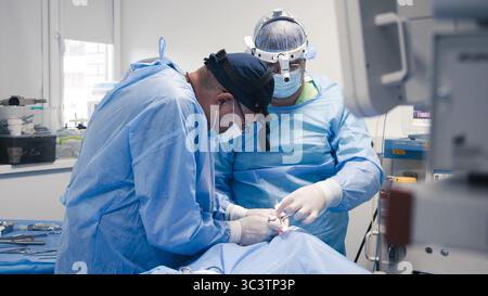 Due operatori sanitari in abbigliamento chirurgico blu sono impegnati in una procedura chirurgica in una sala operatoria sterile Foto Stock