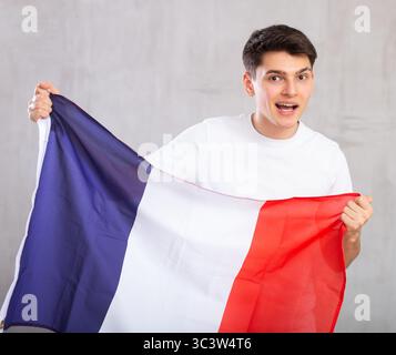 Eccitato, attivo spettatore maschile detiene bandiera nazionale della Francia in mani e canti slogan popolare Foto Stock