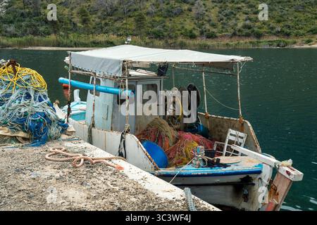 Primo piano di un rustico peschereccio attraccato al porticciolo di Mavrolimni, pieno di colorate reti da pesca e attrezzature contro acque calme. Foto Stock