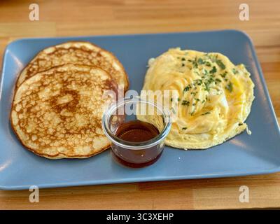 Piatto di soffici frittelle servite con cremose uova strapazzate e un piccolo contenitore in vetro di sciroppo, Lübeck, Germania. Foto Stock