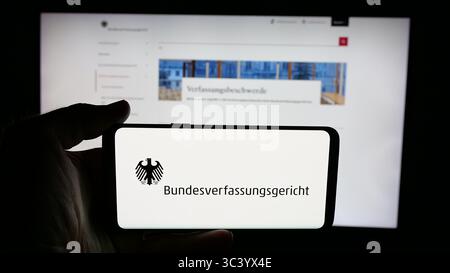 Stoccarda, Germania - 06-11-2025: Persona che tiene il cellulare con il logo del tribunale Bundesverfassungsgericht (BVerfG) sullo schermo di fronte alla pagina web. Foto Stock
