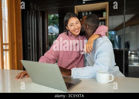 Felice coppia multietnica che utilizza un notebook, acquista online con le vendite, gioca insieme Foto Stock