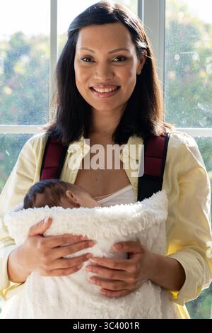 Madre asiatica negli anni '30 che tiene il neonato in una lussuosa coperta utilizzando il portapacchi anteriore dalla finestra illuminata dal sole Foto Stock