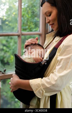 Madre afroamericana che tiene il bambino dormiente in un portabagagli nero, con finestra di legno rivestita, spazio fotocopie Foto Stock
