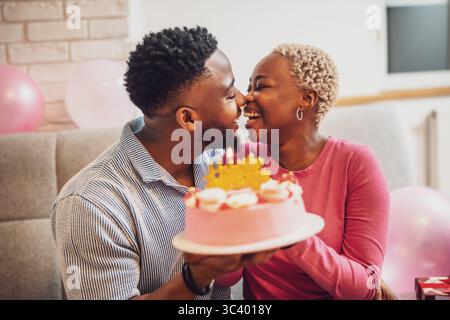 Felice giovane coppia che festeggia il compleanno della donna a casa. Stanno tenendo la torta con la candela di compleanno e sorridono. Foto Stock