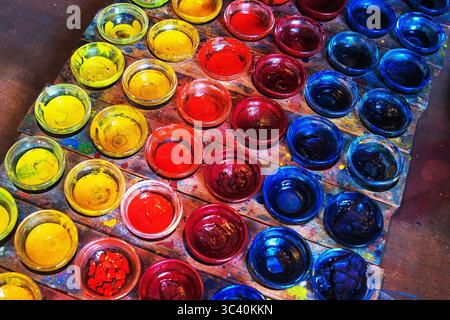 Un set ordinato di ciotole a pigmenti in vetro mostra una gamma vivace di colori primari giallo, rosso e blu su un vassoio di legno Foto Stock