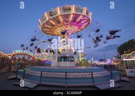Giostra colorata illuminata in una fiera di fronte a un cielo notturno, giostra a catena, festival primaverile, Cannstatter Wellenflug, illuminata, ora blu Foto Stock