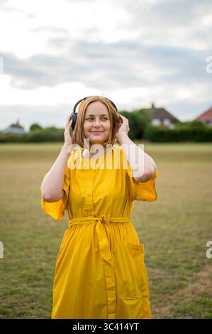 Donna allegra di mezza età che indossa un abito giallo con le cuffie Foto Stock