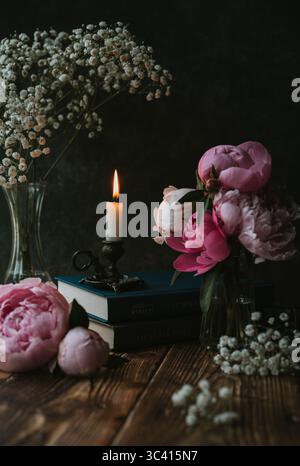 Natura morta con luce bassa con candele, fiori e libri su un tavolo di legno. Foto Stock