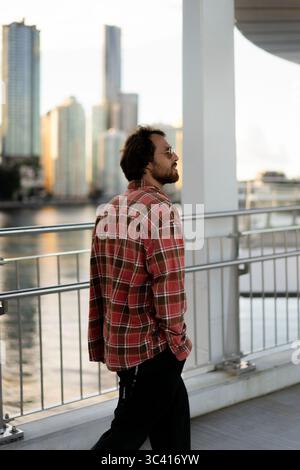 Uomo che cammina su un ponte cittadino, indossa una camicia a quadri e occhiali da sole Foto Stock