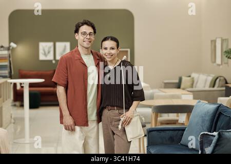 Giovane uomo caucasico adulto e giovane donna caucasica adulta in piedi insieme sorridendo in un negozio di mobili, entrambi guardando la macchina fotografica, mostrando espressione amichevole e postura informale Foto Stock