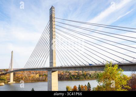 Moderno ponte stradale sospeso sostenuto da piloni di cemento che si estendono su un fiume con sponde boscose nel Maine in un giorno d'autunno soleggiato Foto Stock