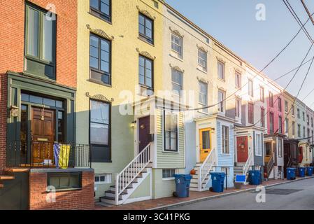 Vecchie case a file in mattoni color pastello con rampe di fili che conducono alle porte frontali in legno lungo una strada al tramonto in autunno Foto Stock