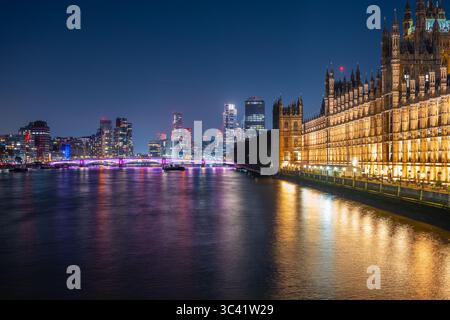 Il Palazzo di Westminster, illuminato e maestoso di notte, si erge lungo il fiume Tamigi, con i moderni grattacieli Vauxhall che brillano sullo sfondo, mostrando il vibrante skyline di Londra. Foto Stock