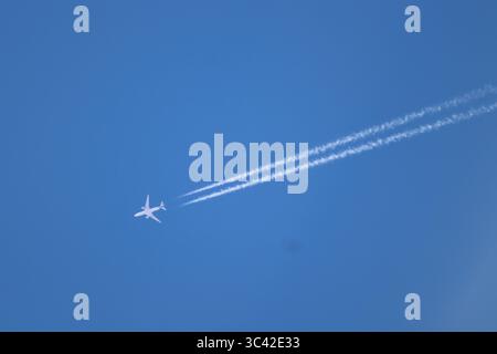 Un jet attraversa il cielo azzurro, lasciando dietro di sé due nitidi contrasti che si estendono sullo sfondo come silenziose tracce di velocità e potenza. Foto Stock