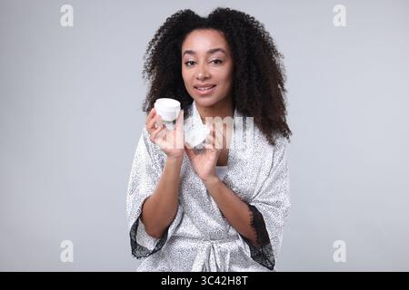 Bella donna brasiliana con barattolo di crema di collagene su sfondo grigio Foto Stock