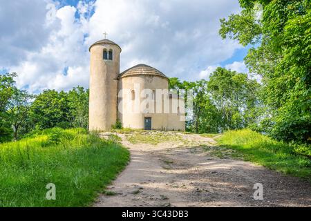 La rotonda romanica di Saint George si trova in cima al monte Rip, circondata da una vegetazione lussureggiante sotto un cielo blu luminoso, che mostra l'architettura storica in un tranquillo sfondo naturale. Foto Stock