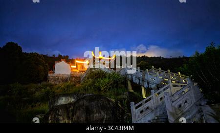 La scena fotografica mozzafiato al tramonto si svolge alle grotte di Batu in Malesia, dove un cielo d'ora d'oro incontra le luci della torre urbana e l'illuminazione notturna della strada. Da Foto Stock