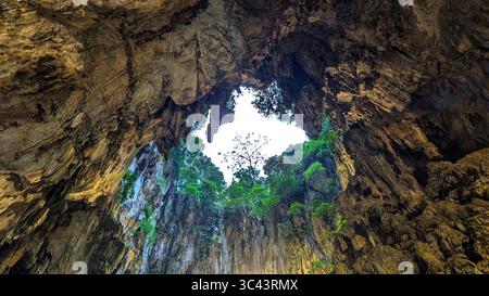 La scena fotografica mozzafiato al tramonto si svolge alle grotte di Batu in Malesia, dove un cielo d'ora d'oro incontra le luci della torre urbana e l'illuminazione notturna della strada. Da Foto Stock