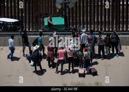 I migranti si riuniscono al confine di Ciudad Juarez, supervisionati da un agente di pattuglia. Foto Stock