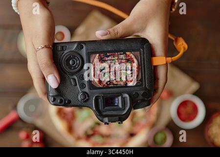 Woman Capturing Overhead Pizza Image with Professional Camera Foto Stock