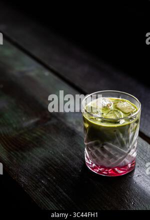 Rinfrescante latte matcha di fragole ghiacciate servito su un tavolo rustico in legno in un'accogliente caffetteria. Bevanda a strati colorata ed estetica, perfetta per un soggiorno Foto Stock