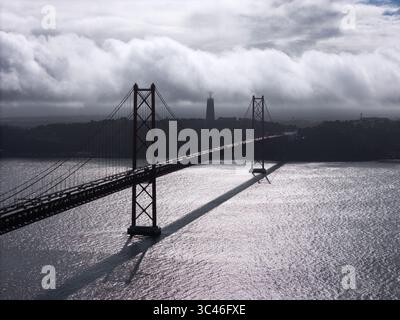 Vista aerea del Ponte 25 de Abril che si estende attraverso il fiume Tago verso la statua del Cristo Rei sotto un cielo spettacolare, Lisbona, Lisbona, porto Foto Stock