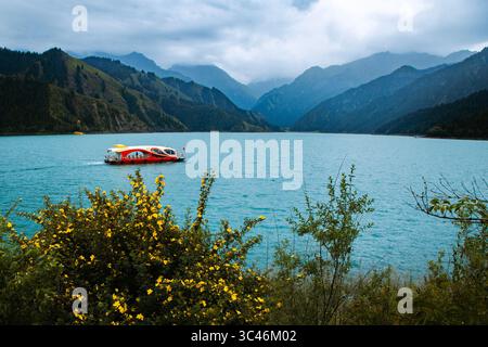 Bellezza serena del lago Tianchi: Barca alla deriva tra i fiori selvatici nelle montagne Tianshan Foto Stock