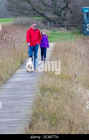 In una giornata grigia allo Snape Maltings nel Suffolk sul fiume ALDE Babbo Natale sta arrivando e papà e figlia camminano un cockapoo mentre aspettano. Foto Stock