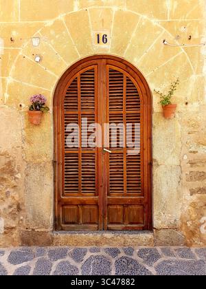 Un'invitante porta in legno antica con un arco arrotondato incastonato in un muro di pietra naturale, che mostra il classico stile mediterraneo Foto Stock