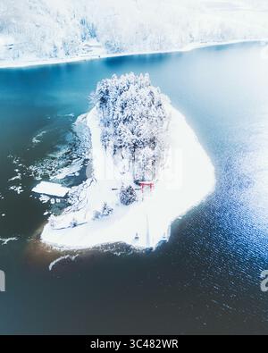 Vista aerea di un'isola innevata con un cancello torii rosso tra le acque scure e riflettenti del lago Nojiri, Shinano, Nagano, Giappone. Foto Stock