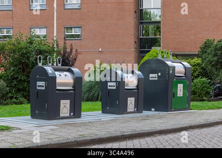 Tre moderni contenitori per rifiuti sotterranei, per diversi tipi di riciclaggio, sono allineati in modo ordinato su un'area pavimentata di fronte a un edificio in mattoni. Utrecht, Foto Stock