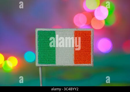 Bandiera irlandese di fronte a luci bokeh multicolore scintillanti, simbolo dell'orgoglio nazionale, dell'indipendenza, dell'eco-turismo e della celebrazione con spirito positivo. Foto Stock