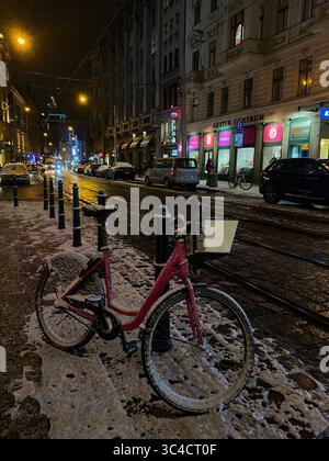 Bicicletta innevata parcheggiata in una strada tranquilla di Praga, Repubblica Ceca, in una notte invernale innevata con lampioni luminosi. Foto Stock