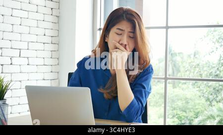 Donna che stringe il braccio sollevato, seduta in posizione non corretta, scrivania da ufficio domestico. Lato posteriore di giovane donna asiatica stanca da lavoro corpo stress mal di schiena ufficio sy Foto Stock