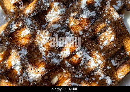 Sfondo con consistenza waffle. Cialde di pasta al cioccolato belga cosparse di zucchero a velo su sfondo bianco. Vista dall'alto. Primo piano. Q. Alta Foto Stock