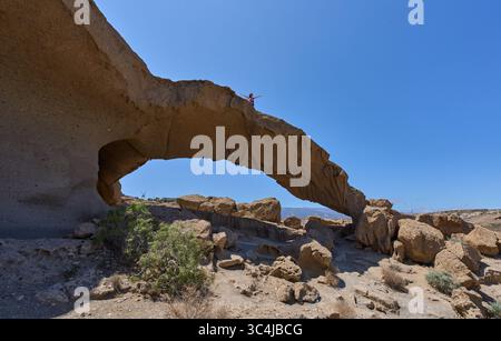 Donna escursionista in piedi sulla cima dell'arco vulcanico di tufo dell'Arco de Tajao con le braccia sollevate nel sud di Tenerife Foto Stock