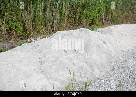 Mucchio di sabbia e ghiaia da costruzione su un'area aperta con piante verdi sullo sfondo. Concetto di materiali da costruzione. Foto Stock