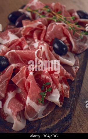 Carne secca appena tagliata, servita con olive ed erbe aromatiche, su un tagliere di legno, nessuno Foto Stock