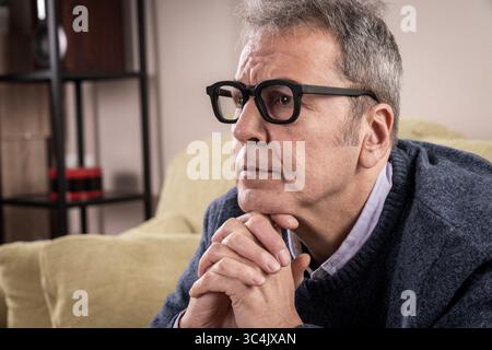Uomo di mezza età con un'espressione penosa e le mani strette, pensando profondamente a una sfida personale o a una strategia aziendale. Foto Stock